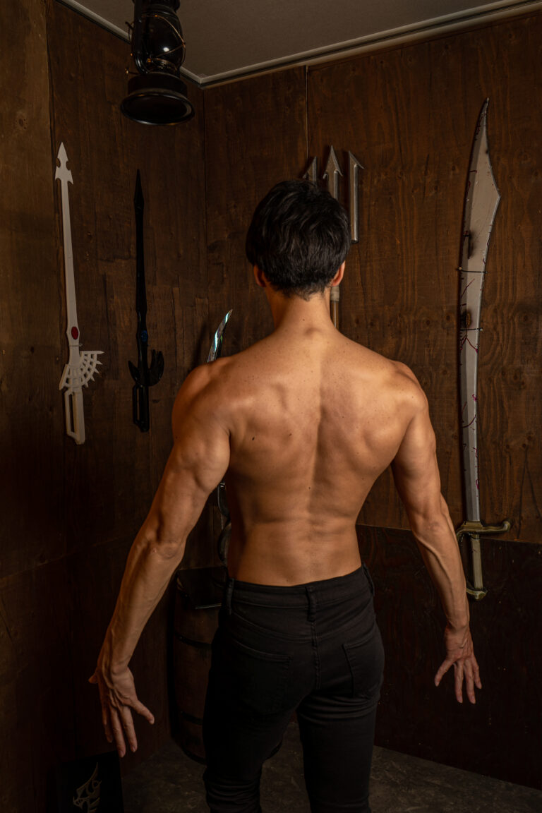 勇者の背中（縦型写真）｜勇者風衣装で背中の筋肉を見せる男性の縦型写真